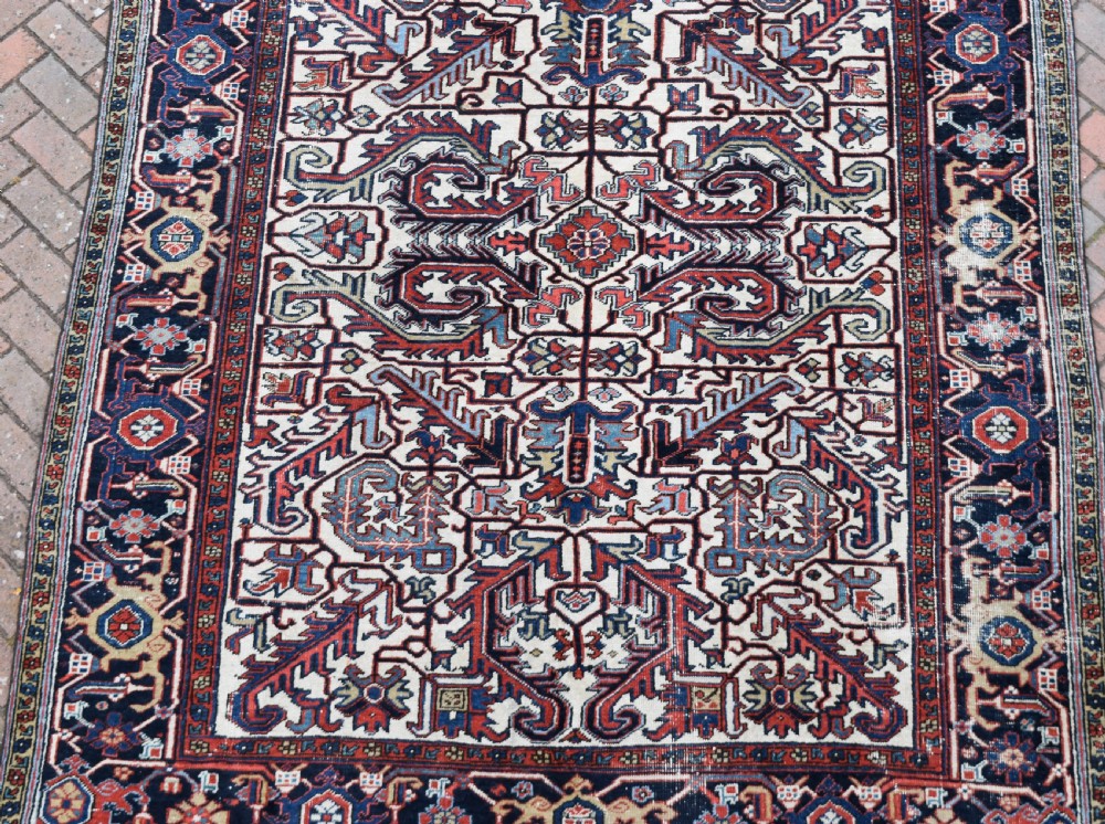 A hand-knotted Heriz wool carpet featuring a large geometric central medallion on an ivory background framed by dark navy floral borders. View II