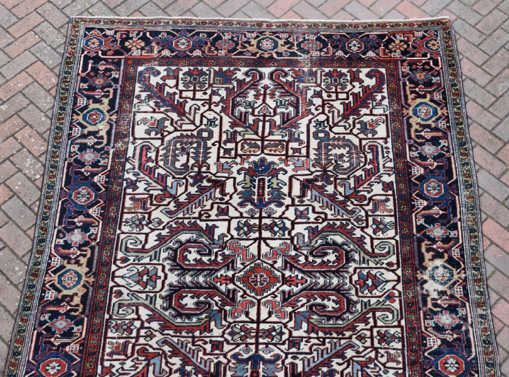A hand-knotted Heriz wool carpet featuring a large geometric central medallion on an ivory background framed by dark navy floral borders. View III