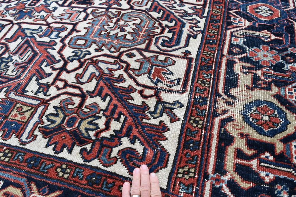A hand-knotted Heriz wool carpet featuring a large geometric central medallion on an ivory background framed by dark navy floral borders. View IV
