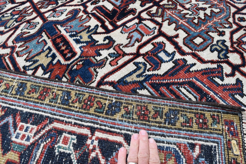 A hand-knotted Heriz wool carpet featuring a large geometric central medallion on an ivory background framed by dark navy floral borders. View VI