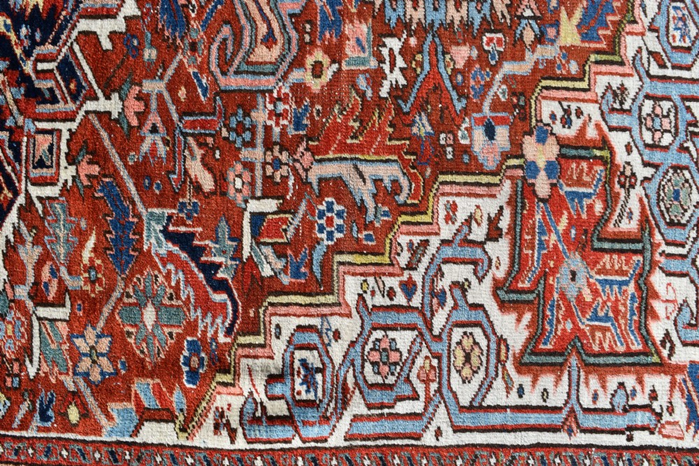 A large hand-knotted antique Heriz wool rug featuring a central geometric medallion in navy blue set against a terracotta red field with intricate corner spandrels. View II