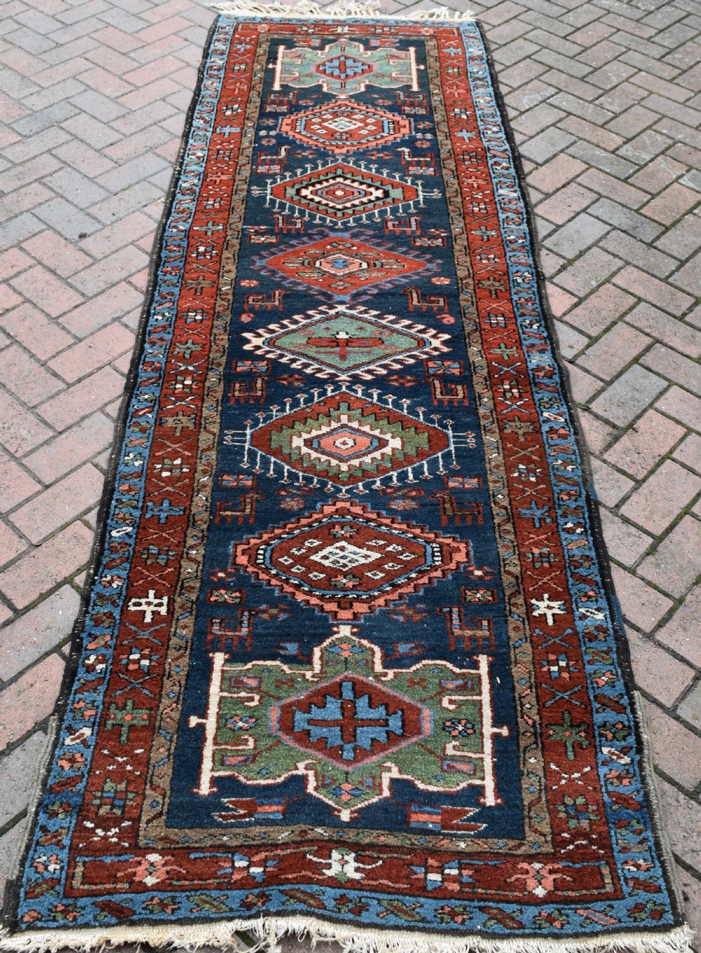 A long hand-knotted Persian Heriz runner rug featuring geometric diamond medallions on a navy blue field with terracotta red borders.