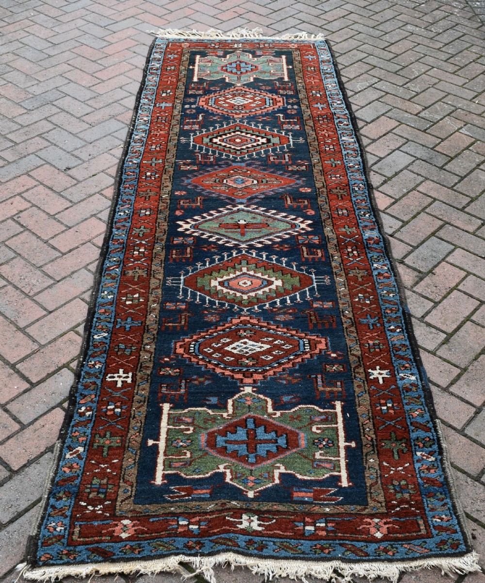 A long hand-knotted Persian Heriz runner rug featuring geometric diamond medallions on a navy blue field with terracotta red borders. View V