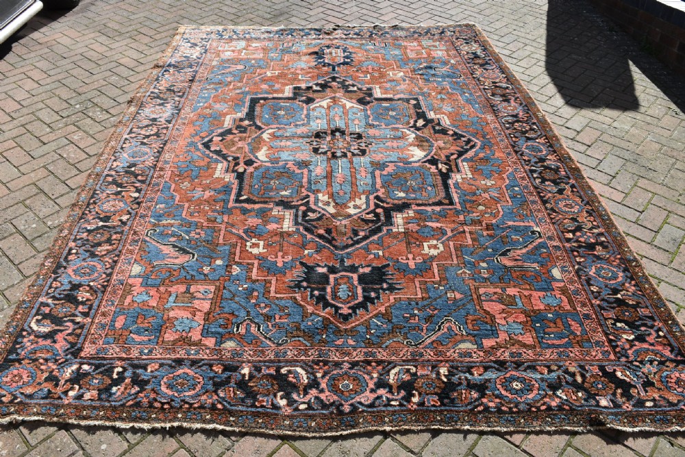 An antique hand-knotted Persian Heriz wool carpet featuring a large sky blue geometric medallion on a terracotta ground surrounded by a dark navy ornate border. View II