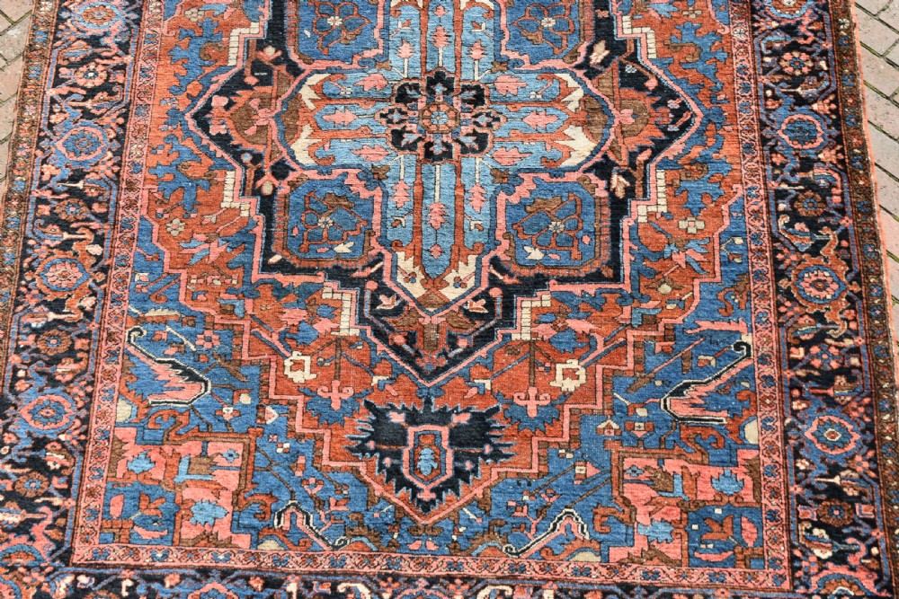 An antique hand-knotted Persian Heriz wool carpet featuring a large sky blue geometric medallion on a terracotta ground surrounded by a dark navy ornate border. View III