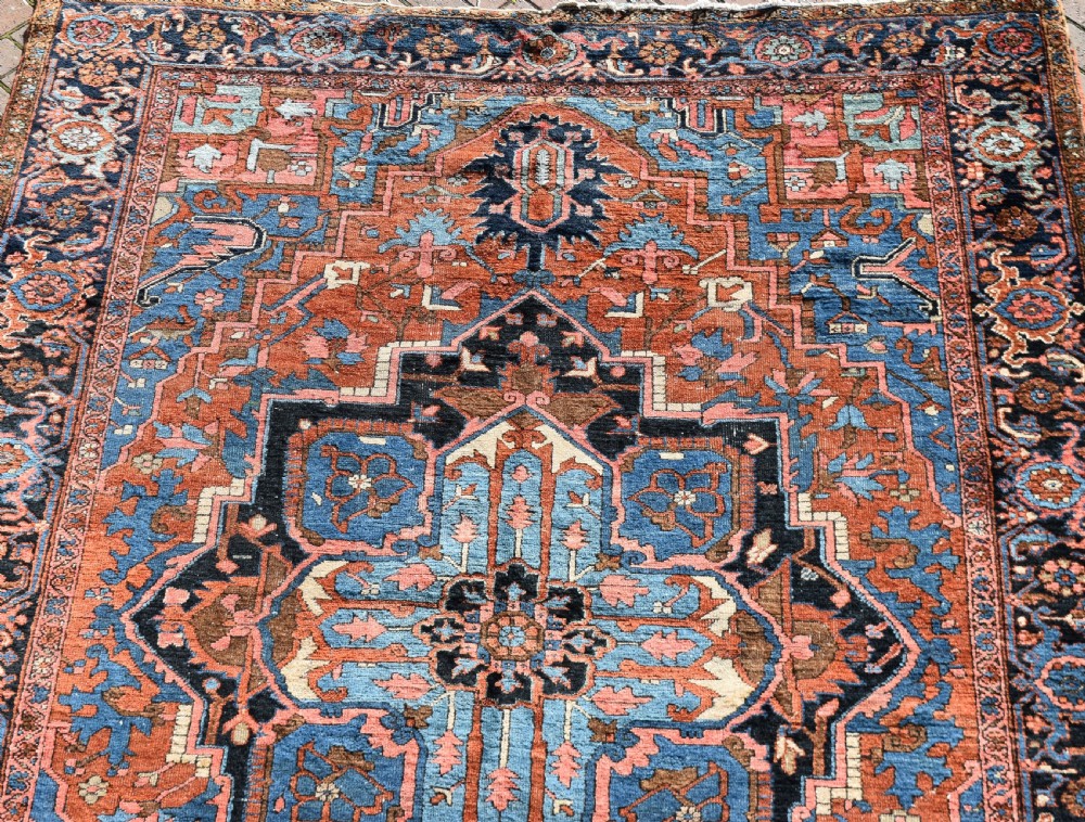 An antique hand-knotted Persian Heriz wool carpet featuring a large sky blue geometric medallion on a terracotta ground surrounded by a dark navy ornate border. View IV