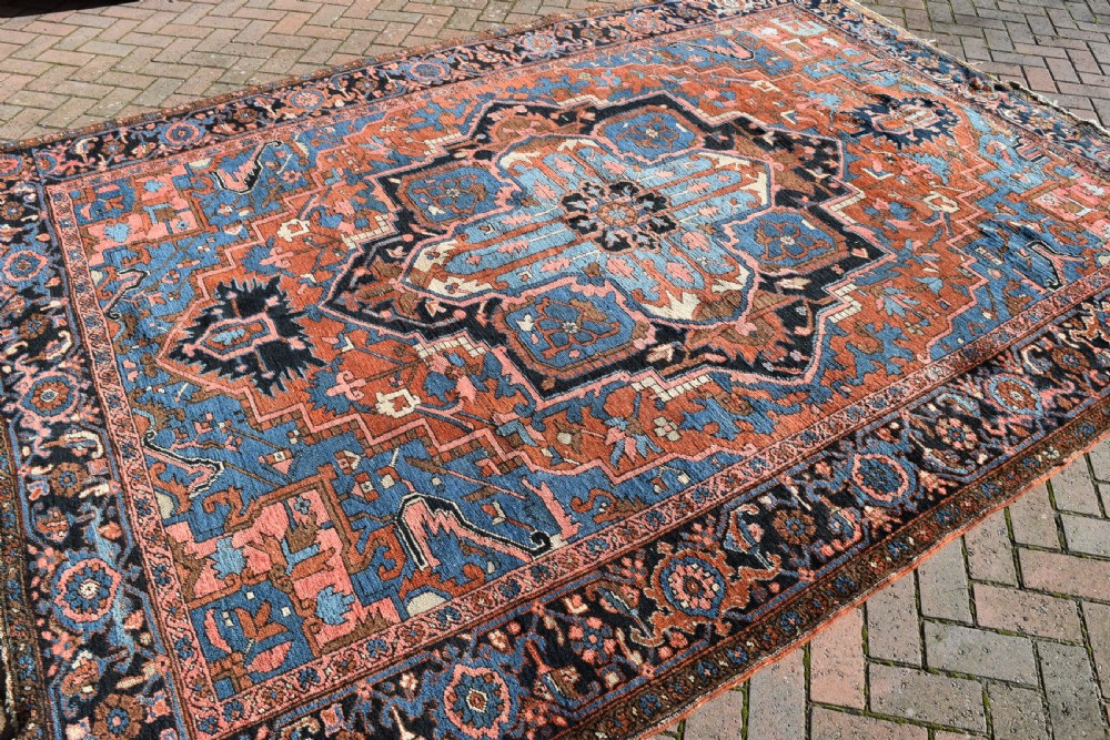 An antique hand-knotted Persian Heriz wool carpet featuring a large sky blue geometric medallion on a terracotta ground surrounded by a dark navy ornate border. View V