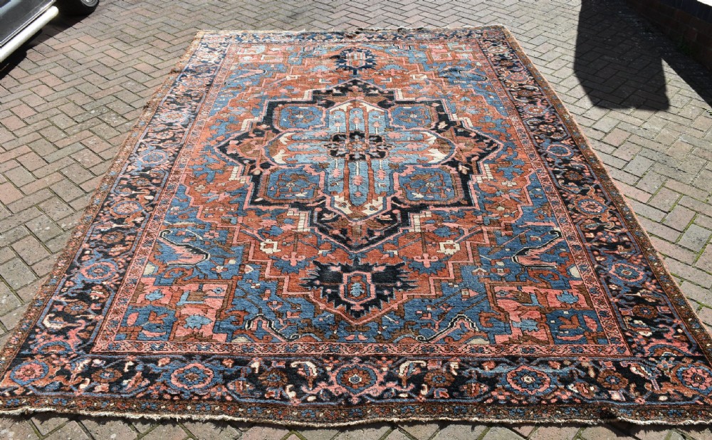 An antique hand-knotted Persian Heriz wool carpet featuring a large sky blue geometric medallion on a terracotta ground surrounded by a dark navy ornate border. View VI