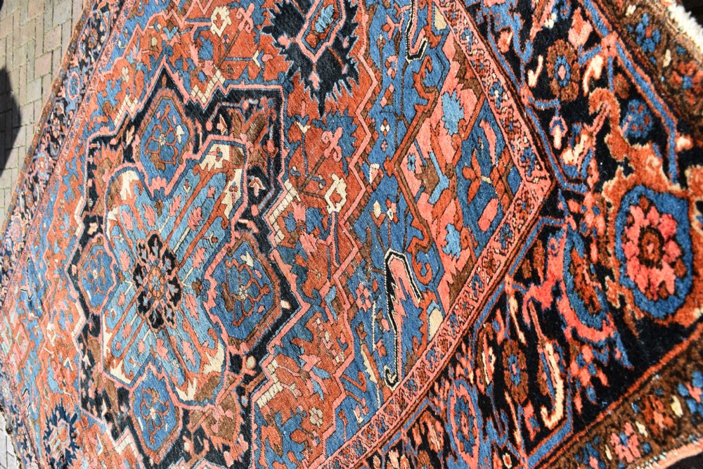 An antique hand-knotted Persian Heriz wool carpet featuring a large sky blue geometric medallion on a terracotta ground surrounded by a dark navy ornate border. View IX