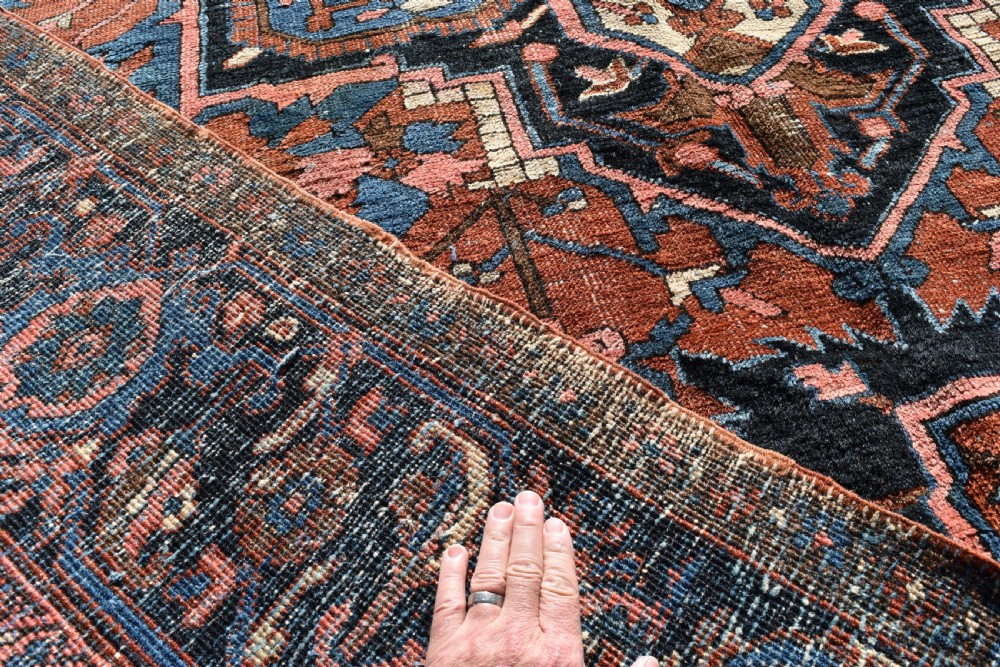An antique hand-knotted Persian Heriz wool carpet featuring a large sky blue geometric medallion on a terracotta ground surrounded by a dark navy ornate border. View X