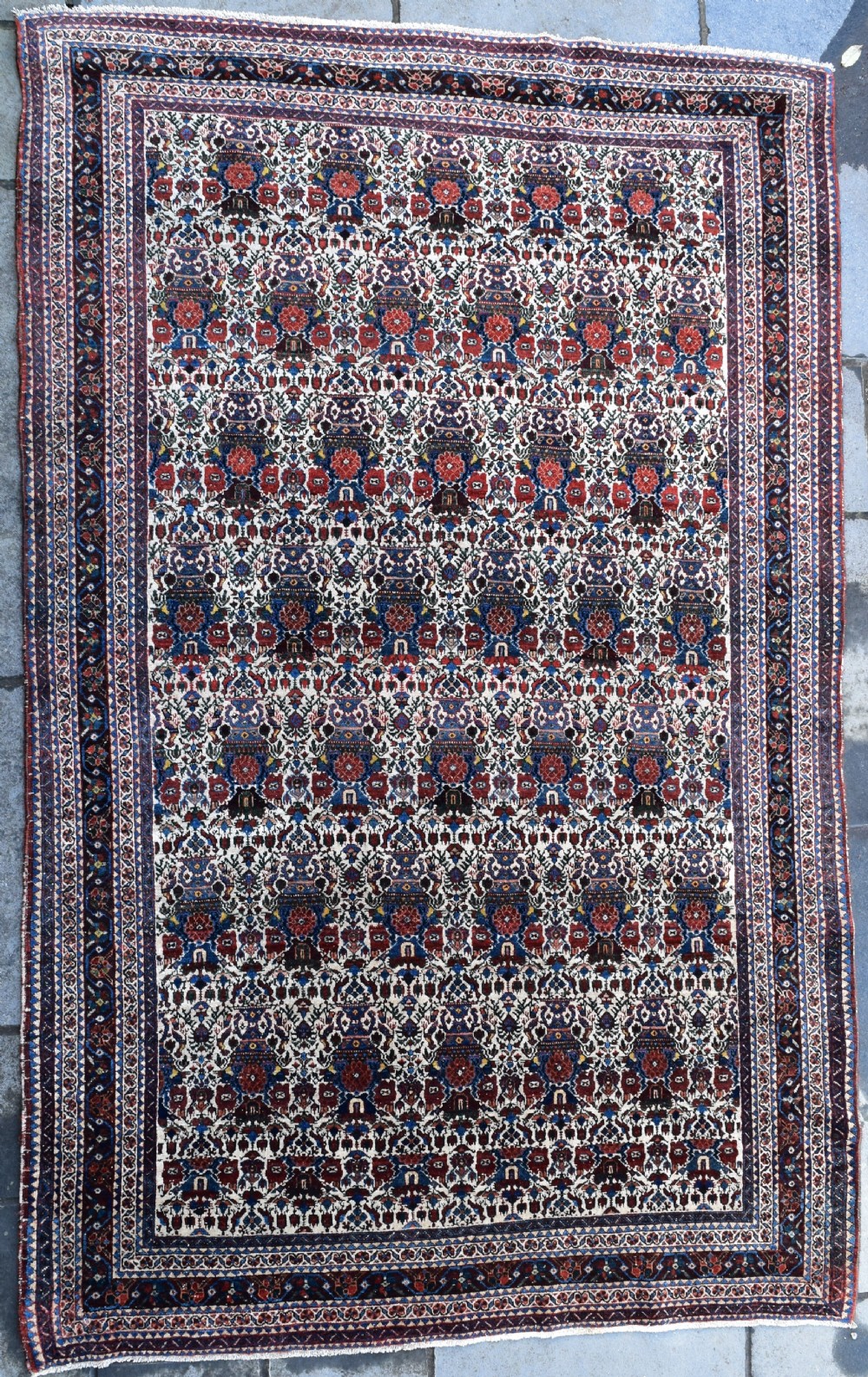 An antique Persian Abadeh hand-knotted wool carpet displaying an intricate repeating floral motif across an ivory field with terracotta and navy borders.