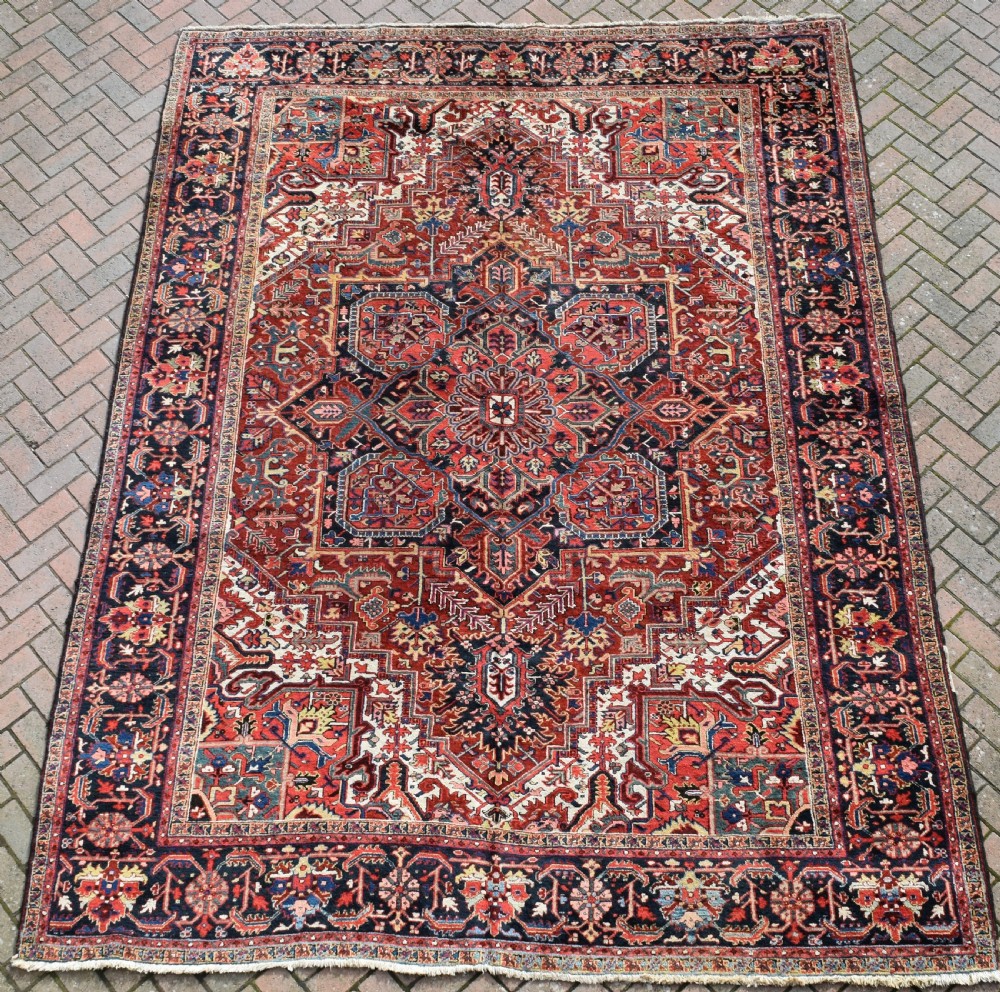 A large hand-knotted Persian Heriz wool carpet featuring a prominent central geometric medallion framed by angular corner spandrels and a multi-tiered decorative border in terracotta, navy, and cream.