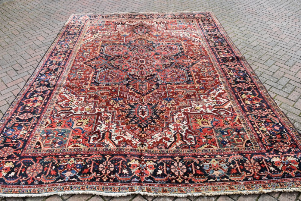 A large hand-knotted Persian Heriz wool carpet featuring a prominent central geometric medallion framed by angular corner spandrels and a multi-tiered decorative border in terracotta, navy, and cream. View II