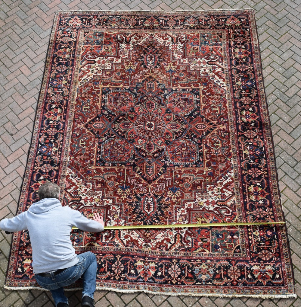 A large hand-knotted Persian Heriz wool carpet featuring a prominent central geometric medallion framed by angular corner spandrels and a multi-tiered decorative border in terracotta, navy, and cream. View IV
