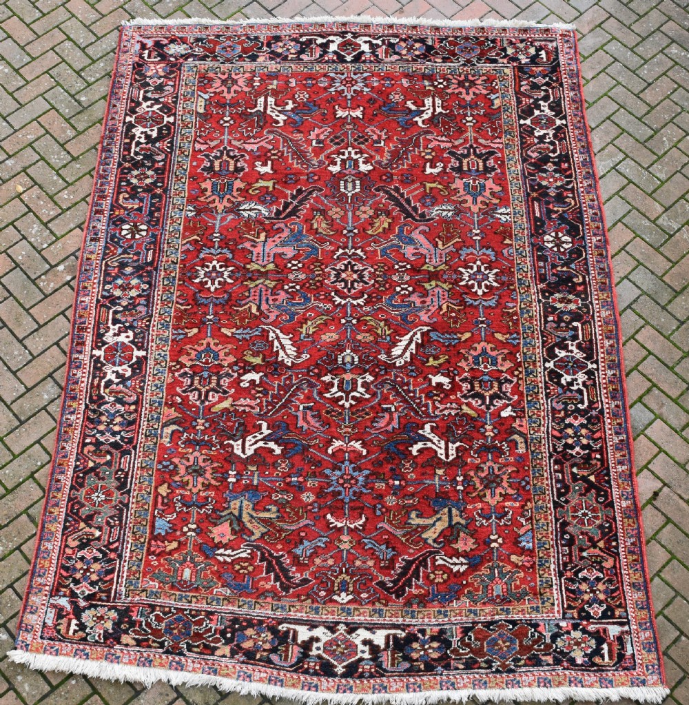 A hand-knotted Persian Heriz wool rug featuring a rich red central field with geometric patterns and a dark navy blue border.