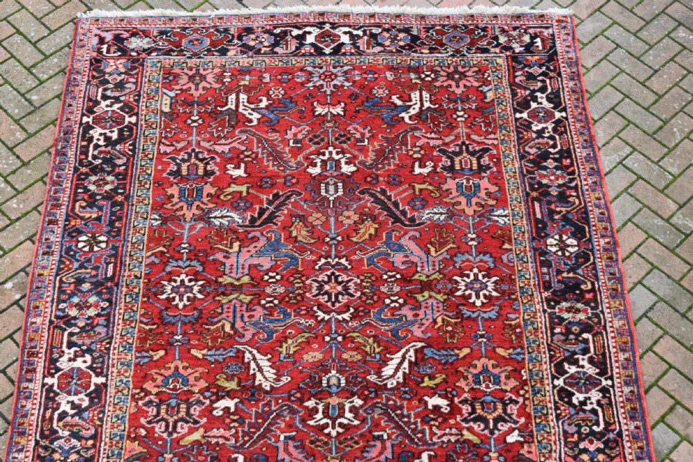 A hand-knotted Persian Heriz wool rug featuring a rich red central field with geometric patterns and a dark navy blue border. View III