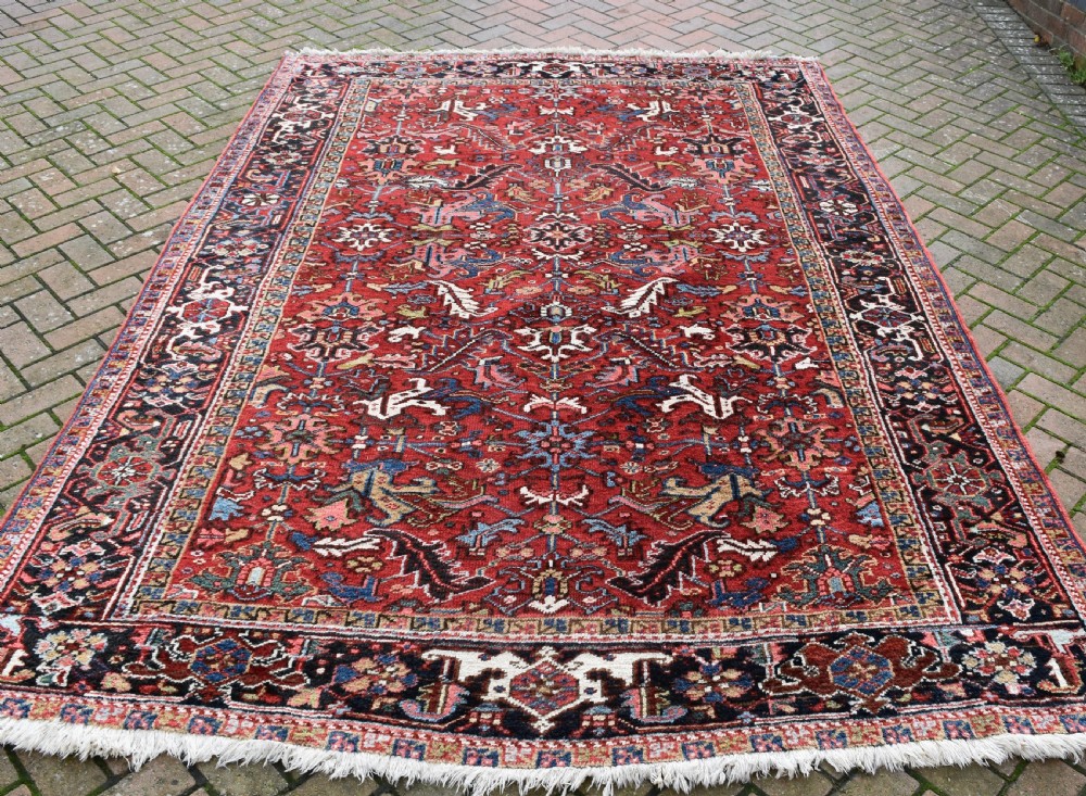 A hand-knotted Persian Heriz wool rug featuring a rich red central field with geometric patterns and a dark navy blue border. View IV