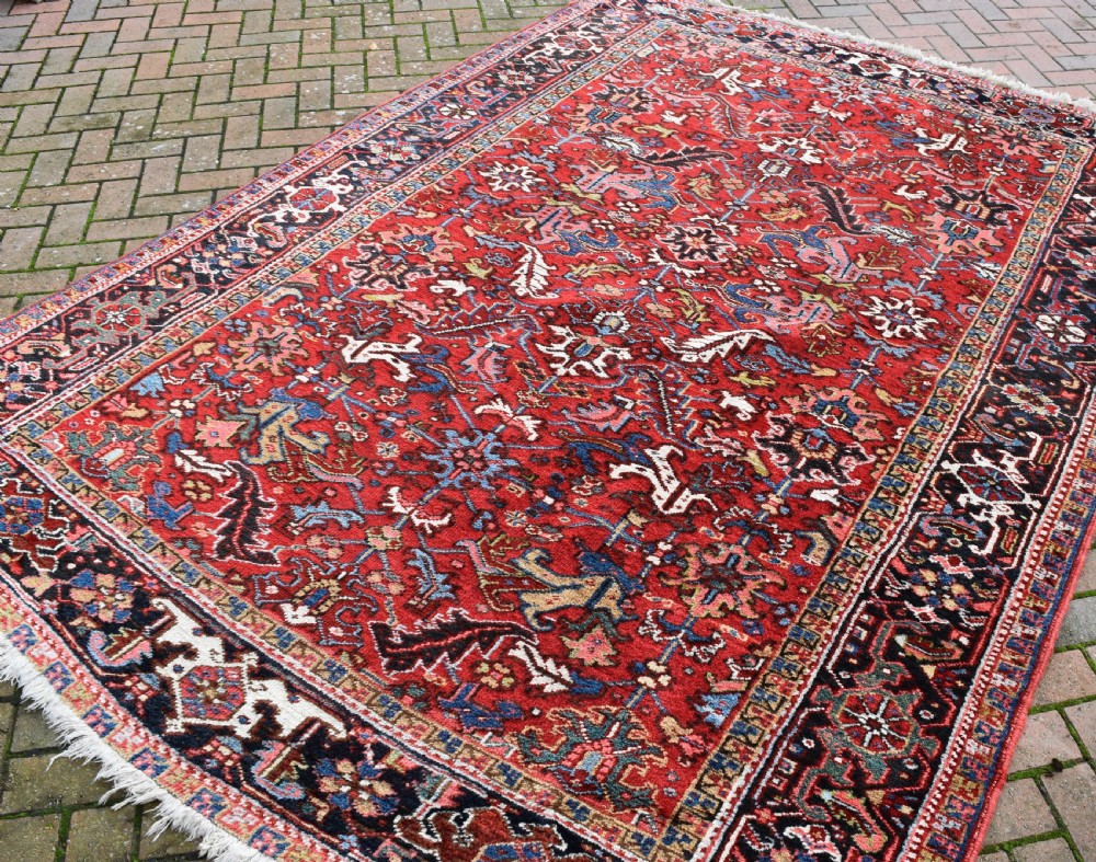 A hand-knotted Persian Heriz wool rug featuring a rich red central field with geometric patterns and a dark navy blue border. View V