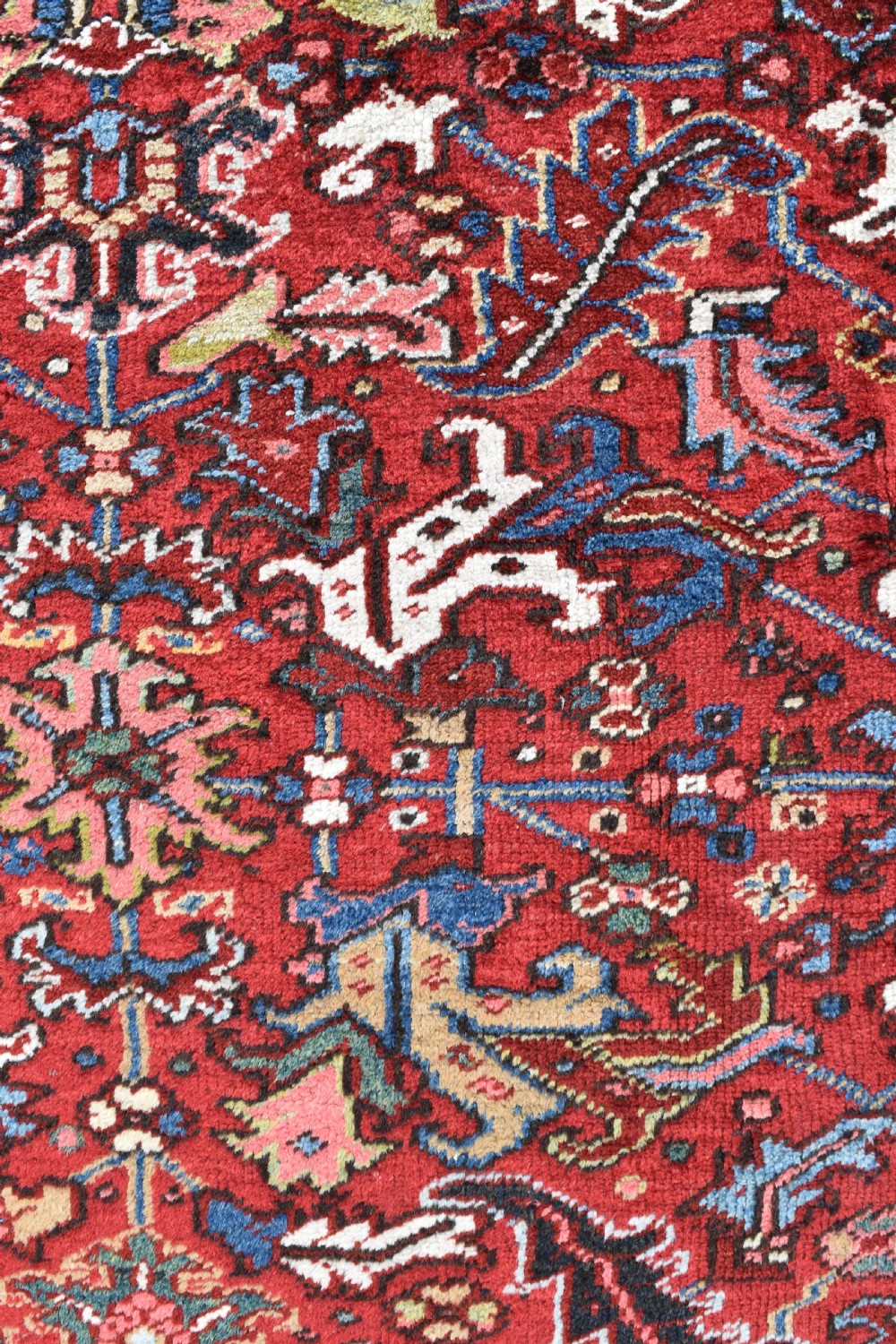 A hand-knotted Persian Heriz wool rug featuring a rich red central field with geometric patterns and a dark navy blue border. View VI