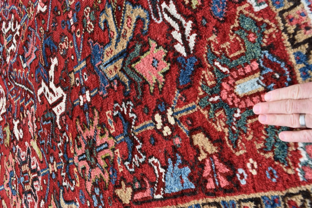 A hand-knotted Persian Heriz wool rug featuring a rich red central field with geometric patterns and a dark navy blue border. View VIII