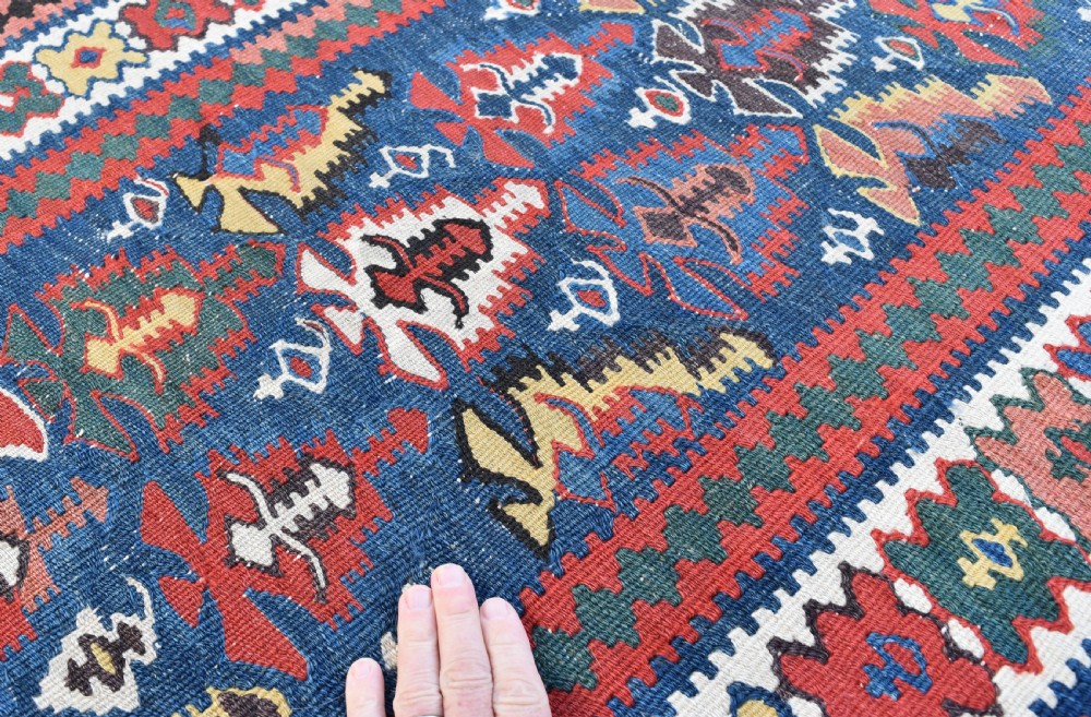 An extra long, hand-woven wool kilim runner rug featuring geometric tribal patterns in navy blue, red, cream, and ochre with fringed ends. View III