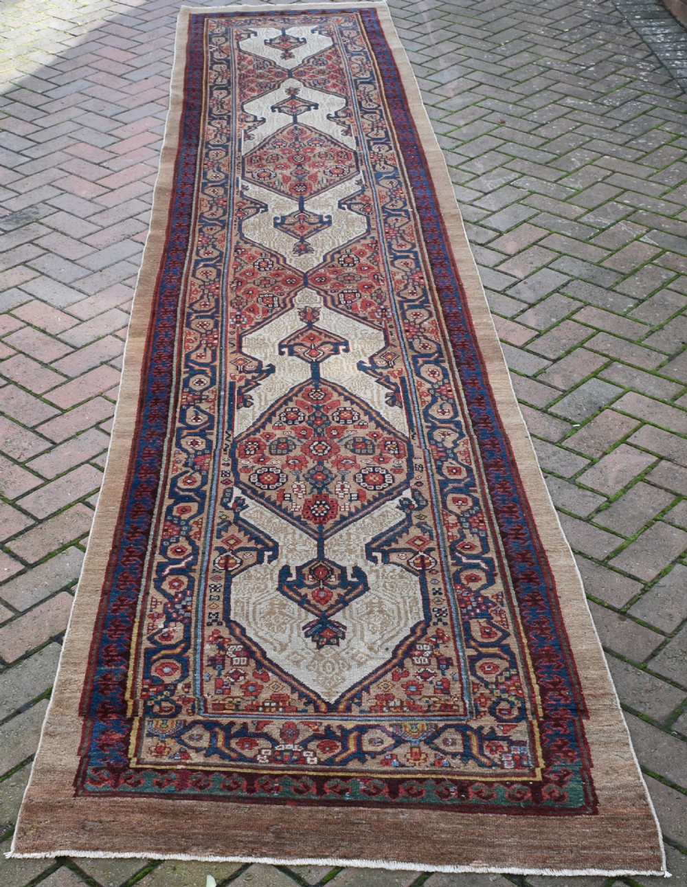 An extra long antique hand-knotted Persian Serab runner rug with geometric diamond medallions on a beige ground with terracotta and indigo accents.