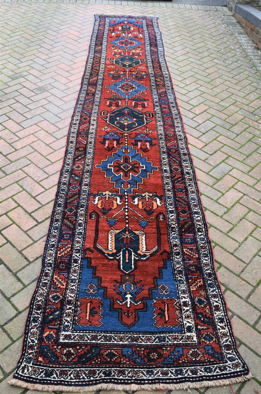 A long, hand-knotted antique Persian wool hall runner featuring geometric blue medallions along a terracotta red field with decorative borders.