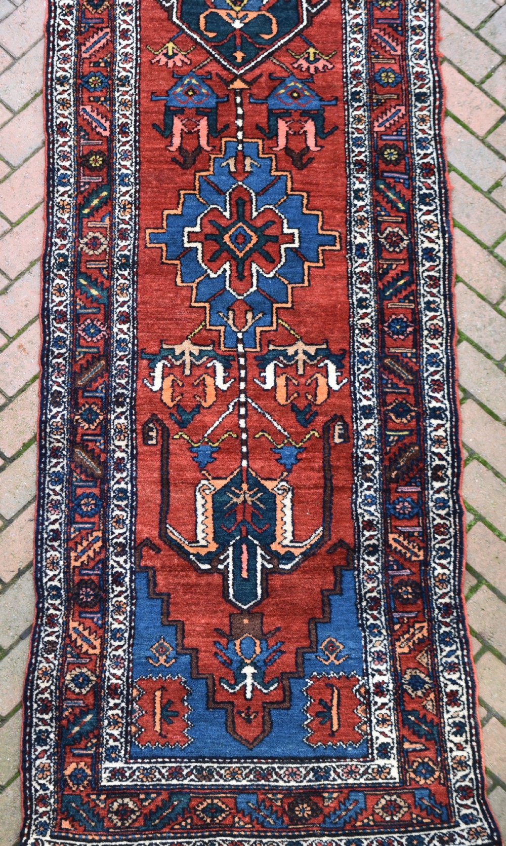 A long, hand-knotted antique Persian wool hall runner featuring geometric blue medallions along a terracotta red field with decorative borders. View II