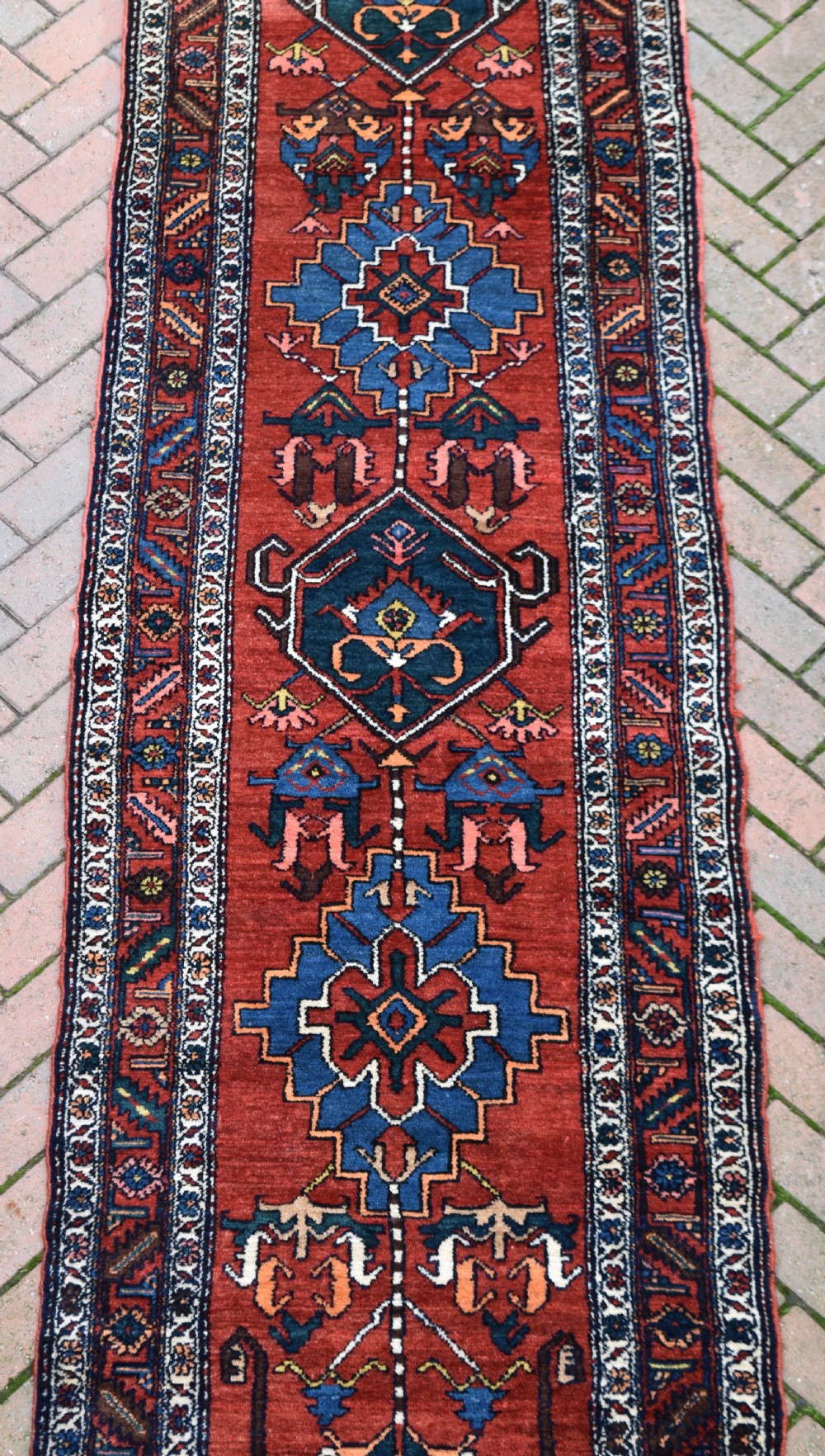 A long, hand-knotted antique Persian wool hall runner featuring geometric blue medallions along a terracotta red field with decorative borders. View III