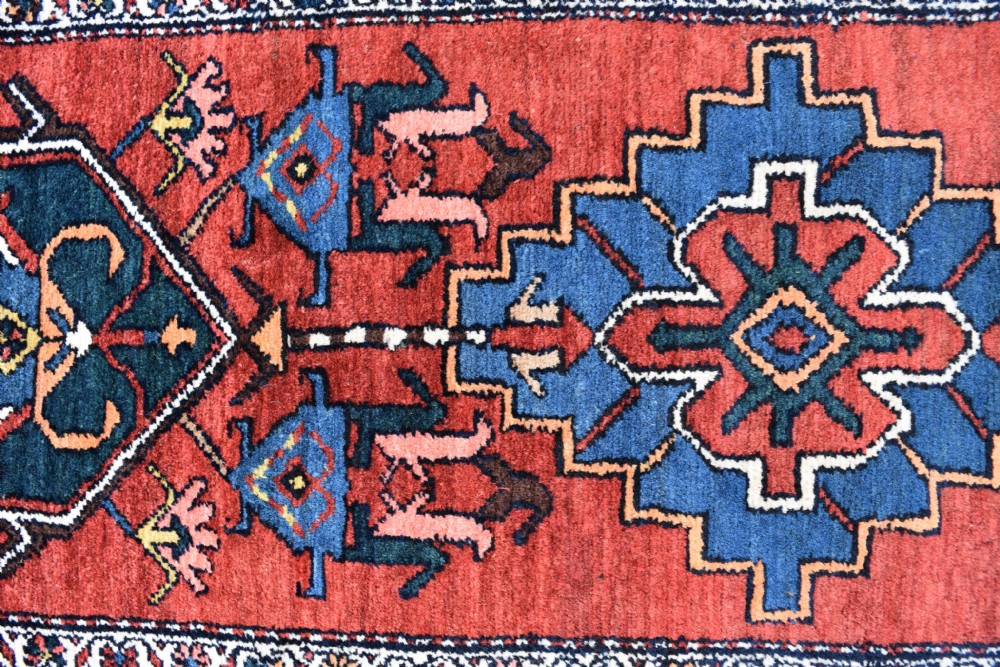 A long, hand-knotted antique Persian wool hall runner featuring geometric blue medallions along a terracotta red field with decorative borders. View VI