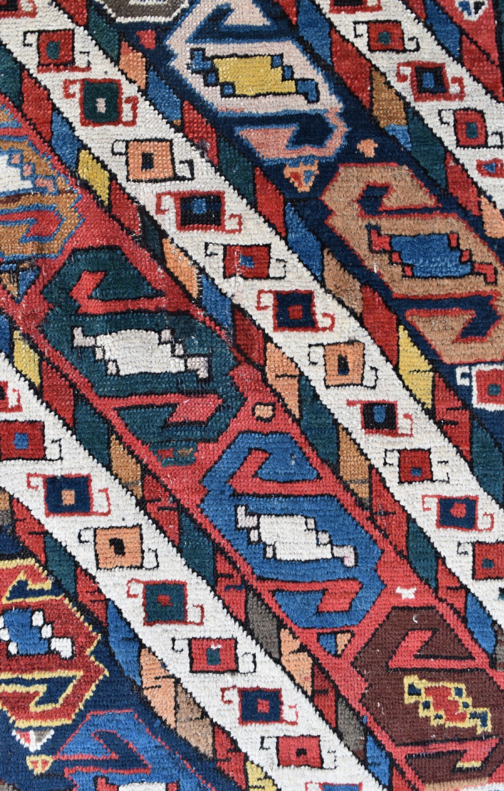 An antique Caucasian Gendje hand-knotted wool runner rug featuring diagonal geometric bands in red, navy blue, yellow, and cream enclosed by a star-motif border. View II