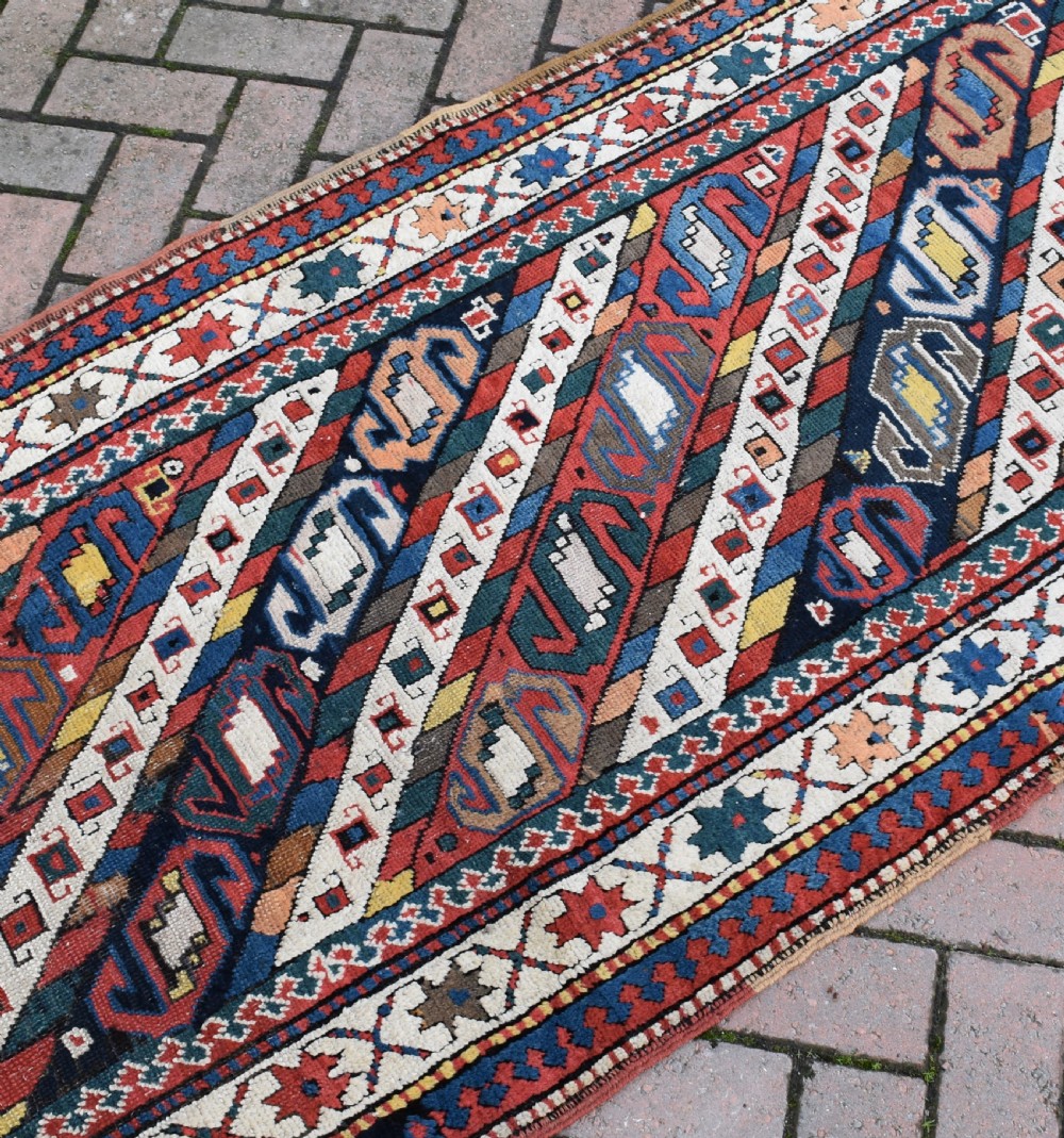 An antique Caucasian Gendje hand-knotted wool runner rug featuring diagonal geometric bands in red, navy blue, yellow, and cream enclosed by a star-motif border. View III