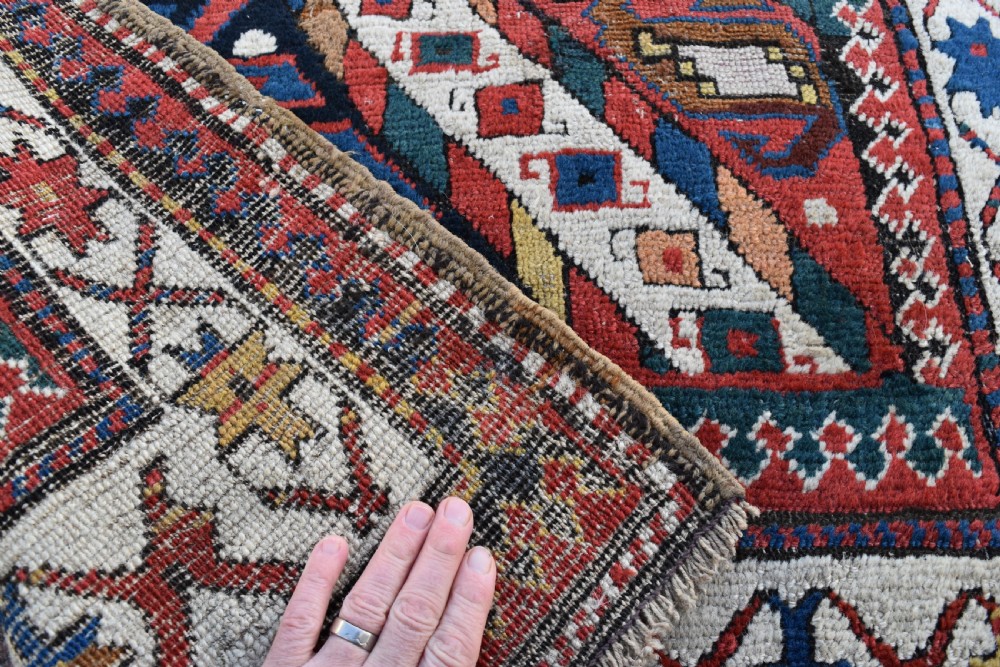 An antique Caucasian Gendje hand-knotted wool runner rug featuring diagonal geometric bands in red, navy blue, yellow, and cream enclosed by a star-motif border. View V