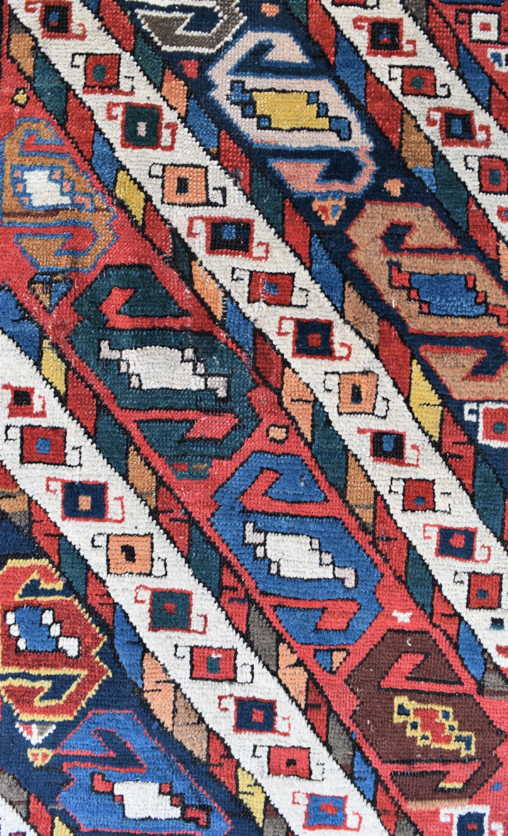 An antique Caucasian Gendje hand-knotted wool runner rug featuring diagonal geometric bands in red, navy blue, yellow, and cream enclosed by a star-motif border. View VI