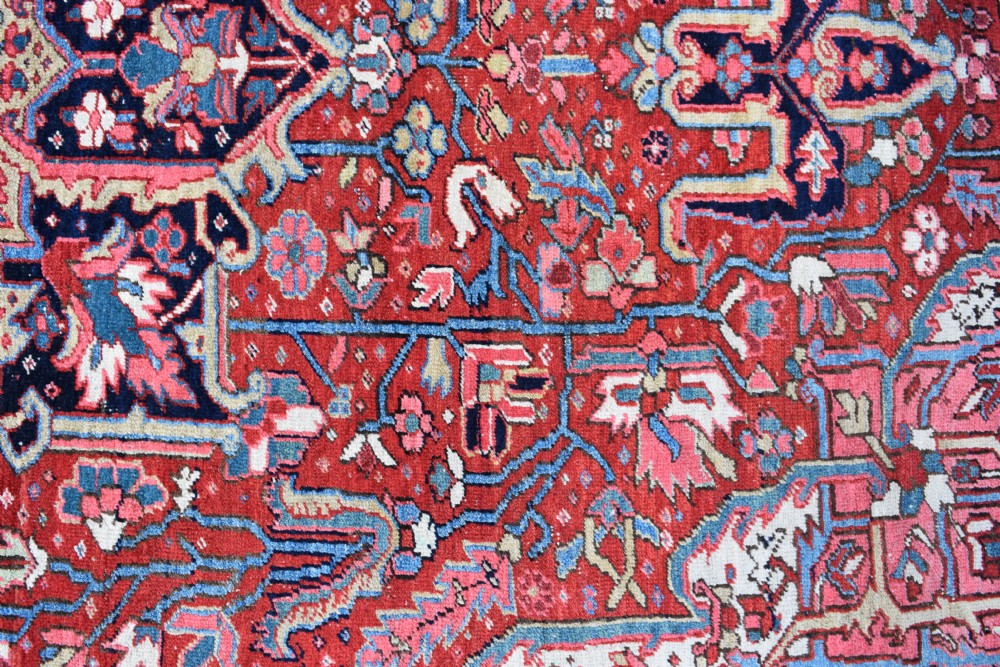 A large hand-knotted Persian Heriz wool carpet featuring a central geometric medallion surrounded by intricate angular motifs in terracotta red, navy blue, and light blue tones. View IV