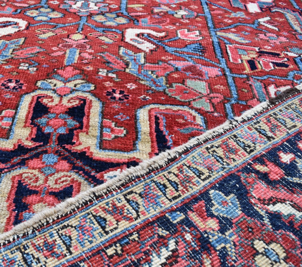 A large hand-knotted Persian Heriz wool carpet featuring a central geometric medallion surrounded by intricate angular motifs in terracotta red, navy blue, and light blue tones. View VIII