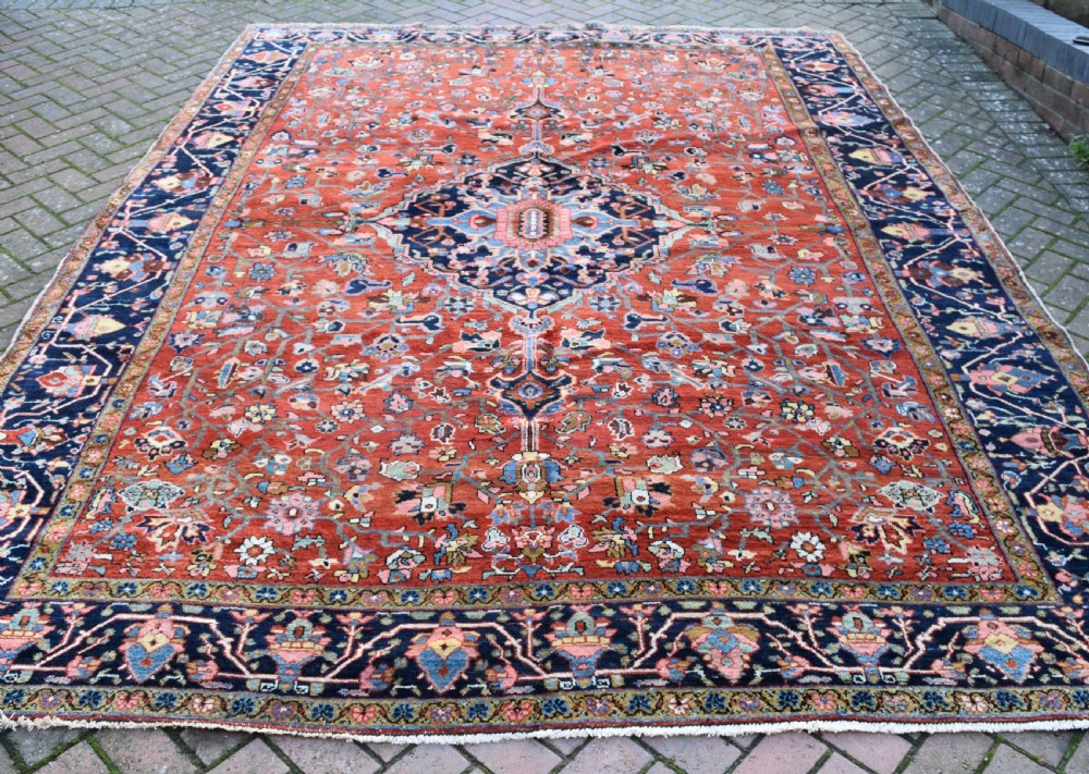 A large hand-knotted Heriz rug with a terracotta red field, central navy star medallion, and dark blue patterned border.
