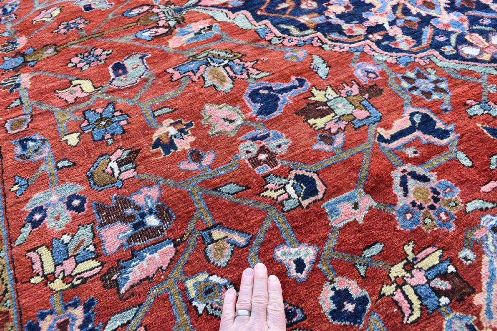 A large hand-knotted Heriz rug with a terracotta red field, central navy star medallion, and dark blue patterned border. View III