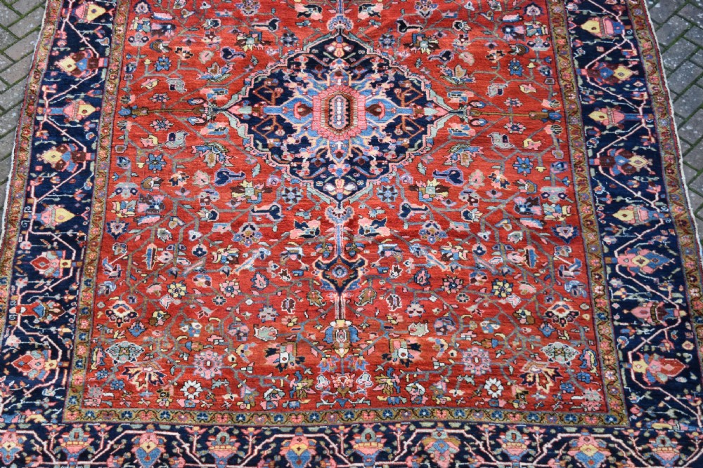 A large hand-knotted Heriz rug with a terracotta red field, central navy star medallion, and dark blue patterned border. View V