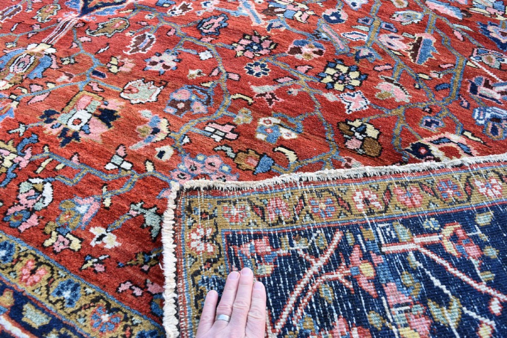 A large hand-knotted Heriz rug with a terracotta red field, central navy star medallion, and dark blue patterned border. View VI