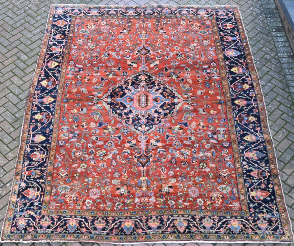 A large hand-knotted Heriz rug with a terracotta red field, central navy star medallion, and dark blue patterned border. View VII