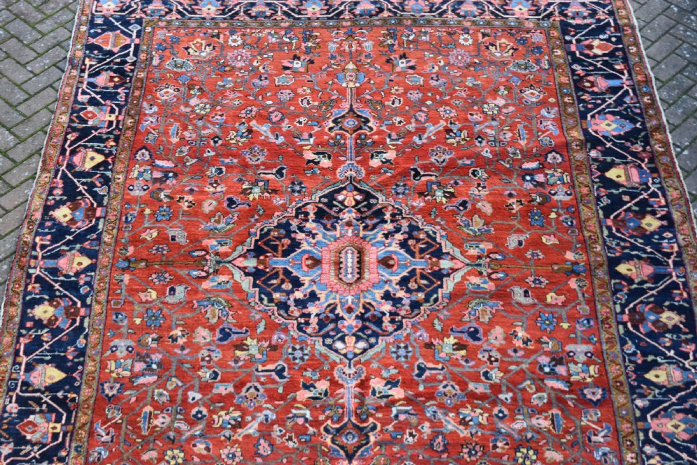 A large hand-knotted Heriz rug with a terracotta red field, central navy star medallion, and dark blue patterned border. View VIII