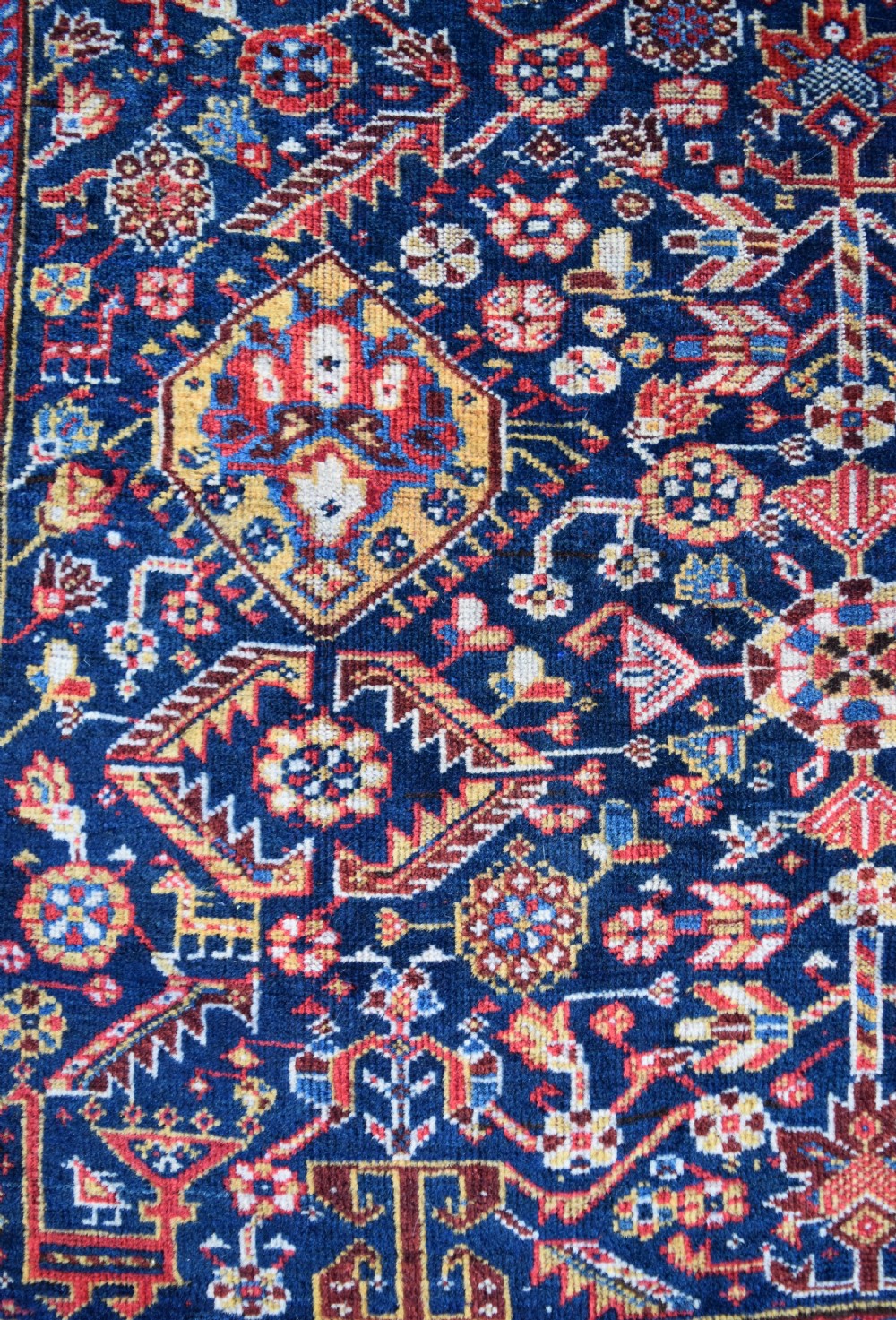 An antique hand-knotted Qashqai wool carpet with a dark navy blue field, central cream and red diamond medallion, and dense geometric border patterns. View II