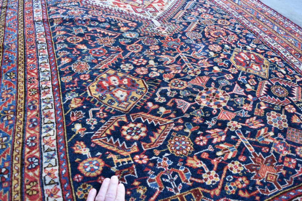An antique hand-knotted Qashqai wool carpet with a dark navy blue field, central cream and red diamond medallion, and dense geometric border patterns. View III