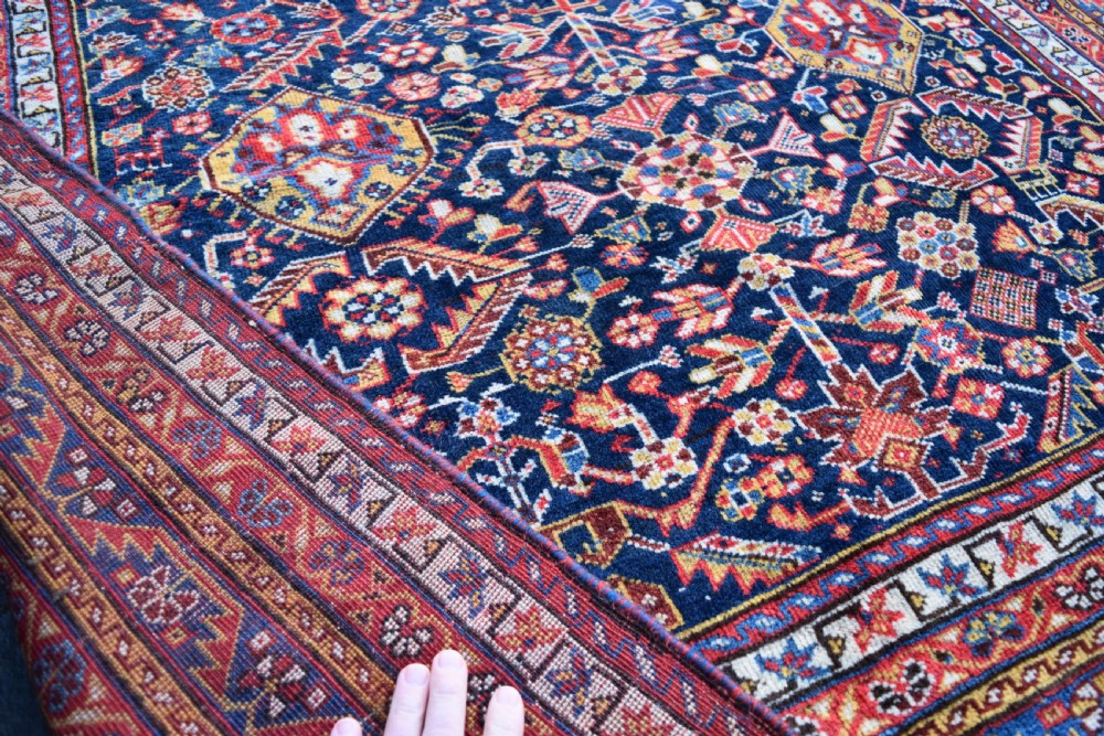 An antique hand-knotted Qashqai wool carpet with a dark navy blue field, central cream and red diamond medallion, and dense geometric border patterns. View IV