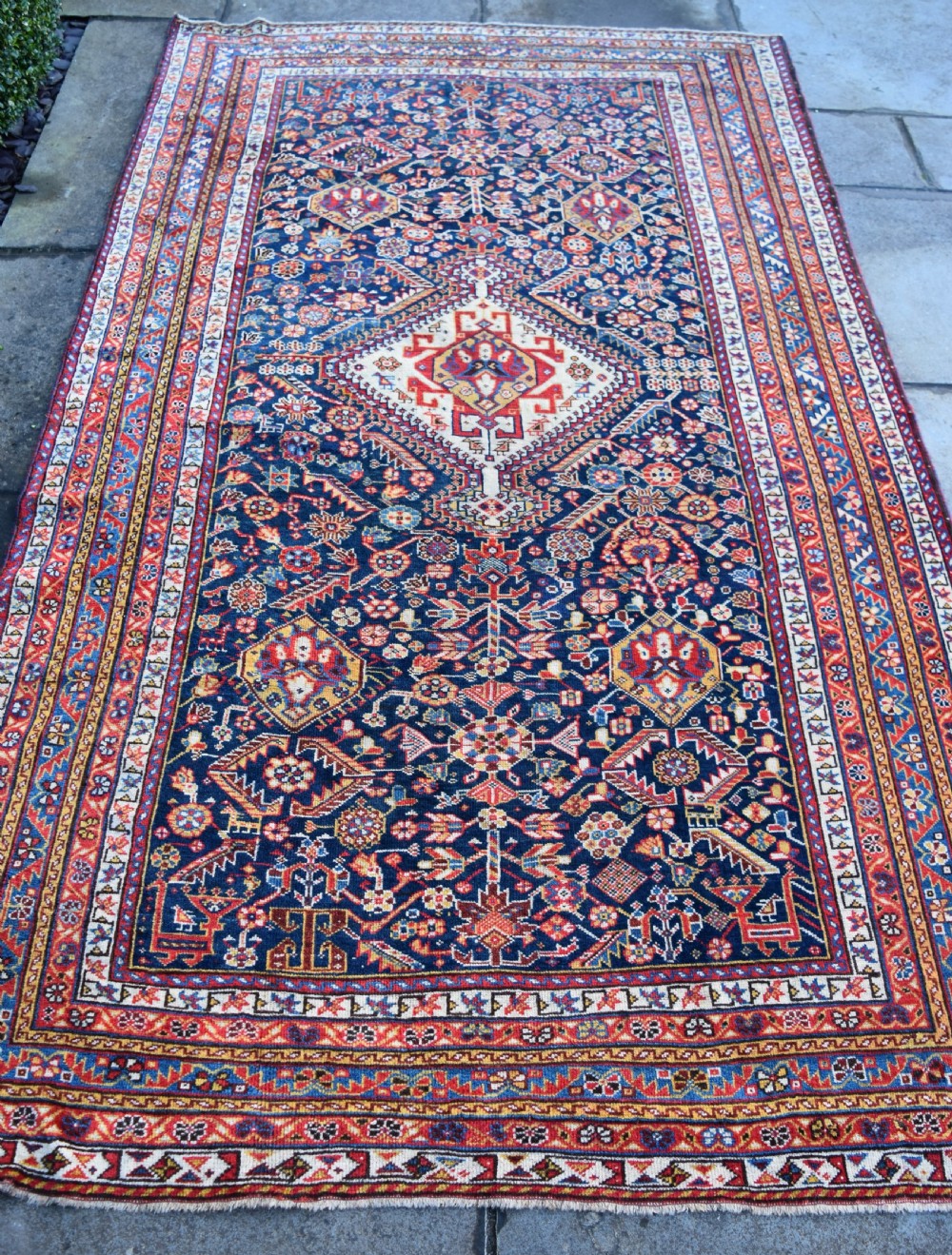 An antique hand-knotted Qashqai wool carpet with a dark navy blue field, central cream and red diamond medallion, and dense geometric border patterns. View V