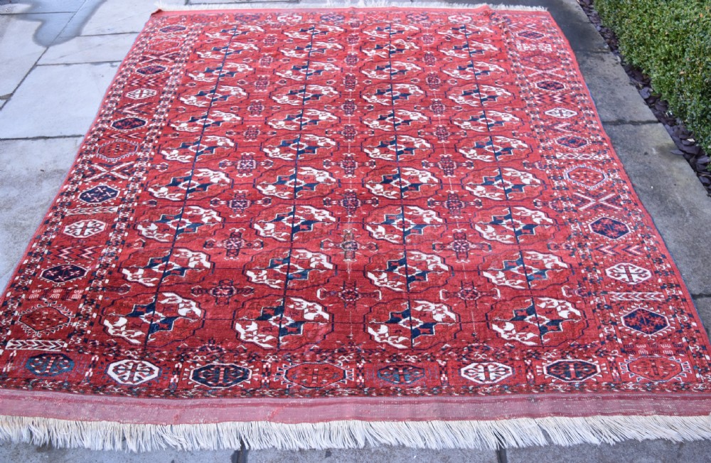 An antique hand-knotted Tekke Turkmen wool carpet featuring a repeating pattern of geometric octagonal guls on a deep red field with decorative geometric borders.