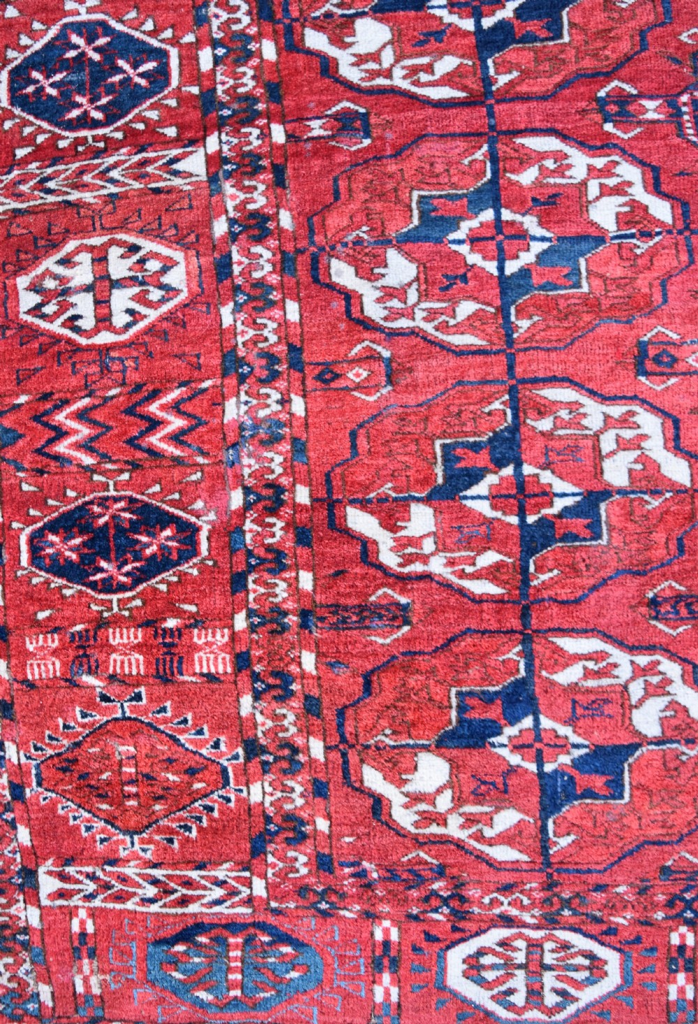 An antique hand-knotted Tekke Turkmen wool carpet featuring a repeating pattern of geometric octagonal guls on a deep red field with decorative geometric borders. View II