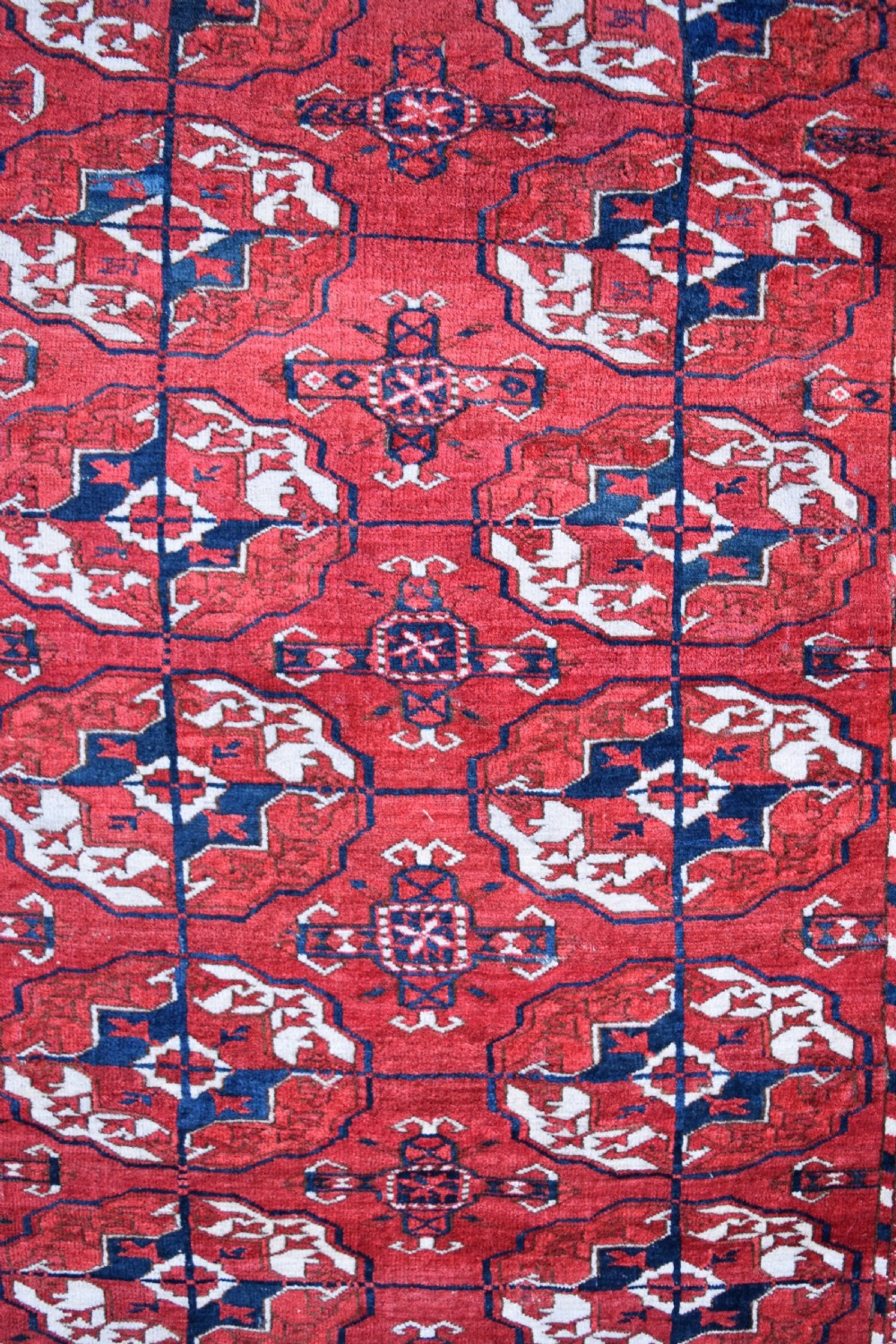 An antique hand-knotted Tekke Turkmen wool carpet featuring a repeating pattern of geometric octagonal guls on a deep red field with decorative geometric borders. View III
