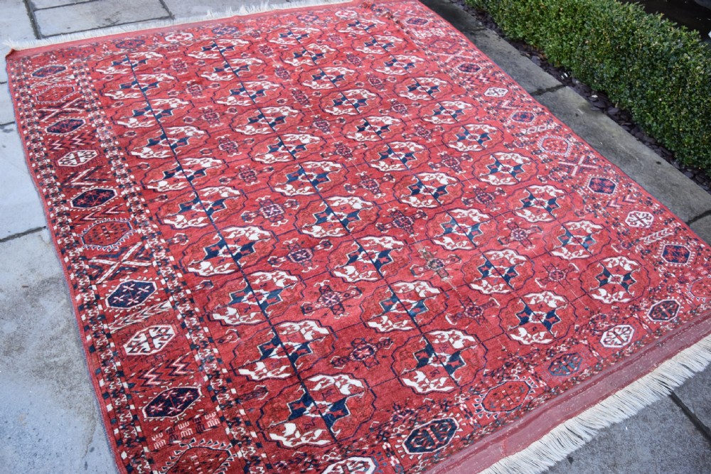 An antique hand-knotted Tekke Turkmen wool carpet featuring a repeating pattern of geometric octagonal guls on a deep red field with decorative geometric borders. View IV